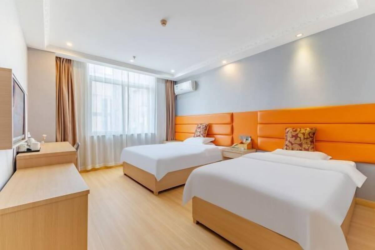 A hotel room with two beds, a desk, a TV, and a window with curtains.