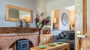 Ein gemütliches Zimmer mit Kamin aus Ziegelsteinen, einem Holztisch mit grünen Blättern, einer Couch und einer großen Wanduhr.