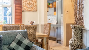 Ein gemütliches Wohnzimmer mit Sofa, Esstisch und Stühlen, eine Küche mit Schränken und einem Kühlschrank, sowie ein dekoratives Wandbild.