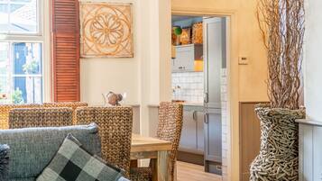 Uma sala de estar acolhedora com sofá, mesa de jantar e cadeiras, cozinha com armários e geladeira, e um detalhe decorativo na parede.