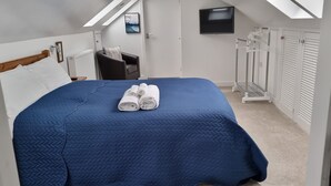Un lit bien fait, recouvert d’une couette bleue, une serviette pliée, une chaise, un téléviseur et un radiateur.