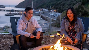 Two people sitting on chairs by a fire pit with a view of a coastal area.