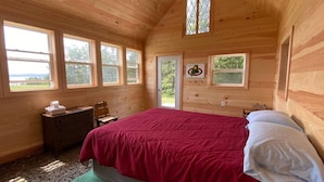 A wooden cabin bedroom with a bed, dresser, and two windows.