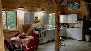 A cabin-style kitchen with white cabinets, a stove, a microwave, and a refrigerator. There is a dining table with chairs and a vase of flowers.