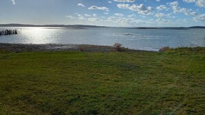 A grassy field with a body of water, a distant shoreline, and a partly cloudy sky.