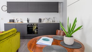 A modern kitchen with dark cabinets, a built-in oven, and a dining area with a round wooden table and a green sofa. - Bootham Row  11 -  a couples retreat that sleeps 3 guests  in 1 bedroom (York)