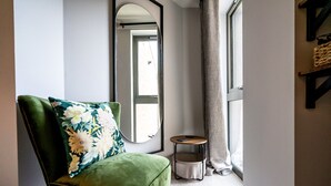 A green armchair with a floral pillow, a round mirror, a small round table, and a window with a curtain. - Bootham Row  11 -  a couples retreat that sleeps 3 guests  in 1 bedroom (York)