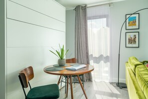 Un salon moderne avec une table ronde en bois, deux chaises, un canapé vert, une plante en pot et des tableaux encadrés accrochés au mur.