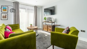 A modern living room with green sofas, a small round table, and a TV mounted on the wall. - Bootham Row  11 -  a couples retreat that sleeps 3 guests  in 1 bedroom (York)