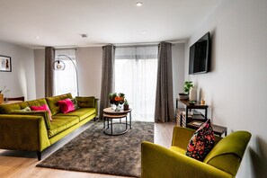 Un salon moderne avec un canapé vert, un fauteuil jaune et une table basse ronde sur laquelle est posé un vase de fleurs.