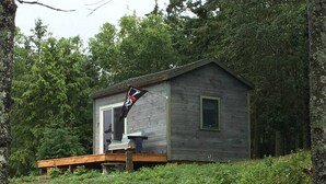 A small wooden cabin with a porch, surrounded by dense forest.