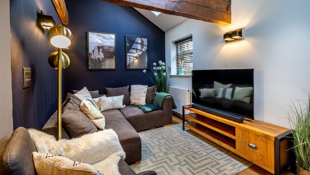Una sala de estar moderna con una pared azul oscuro de acento, un sofá seccional marrón, una lámpara de pie, un mueble de entretenimiento de madera y un televisor de pantalla plana grande.