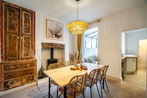Un comedor con mesa de madera, sillas de mimbre, una lámpara colgante y un mueble rústico.