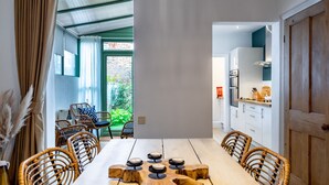 Un comedor con una mesa larga, sillas de mimbre y vistas a un jardín a través de una ventana.