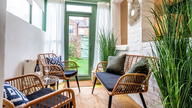 Una habitación acogedora con mobiliario de mimbre, una mesa de cristal y vistas a un jardín a través de una puerta verde.