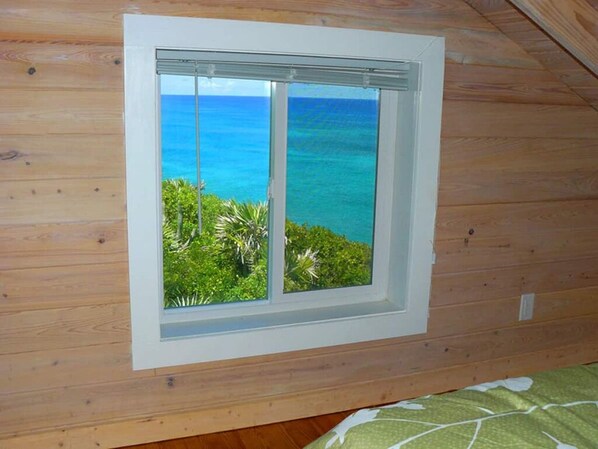 A room with a window overlooking a tropical beach and ocean.
