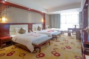 A hotel room with three beds, a wooden headboard, a patterned carpet, and a large window with curtains.