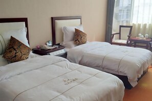 Two beds with white bedding and decorative pillows, a nightstand with a phone and a small table with a cup and saucer.