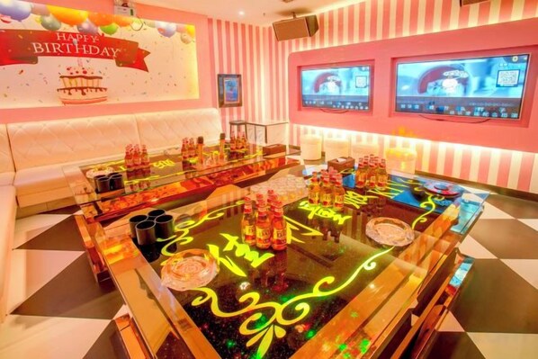 A bar area with a neon-lit table, cushioned seating, and a birthday-themed wall decoration.