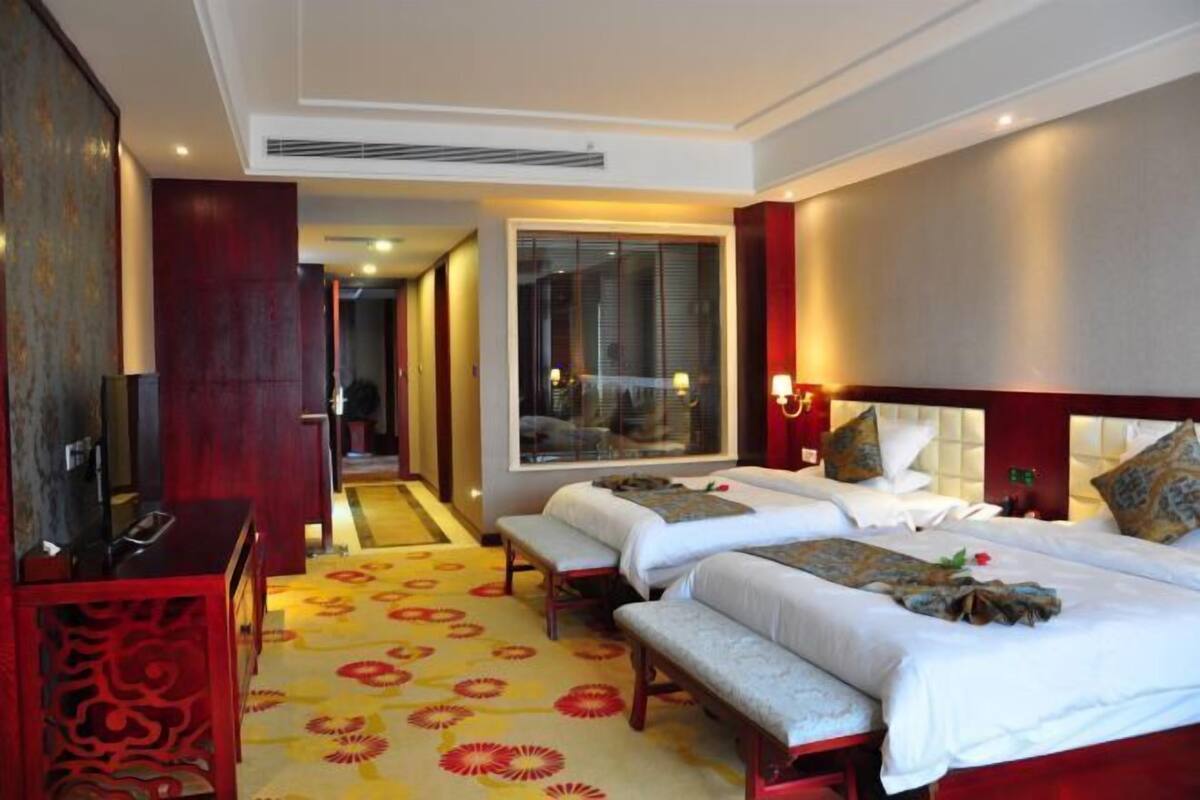 A hotel room with two beds, a desk, and a large window.