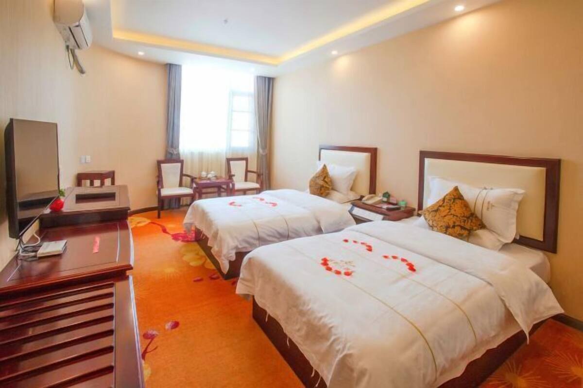 A hotel room with two beds, a desk, a chair, and a TV.