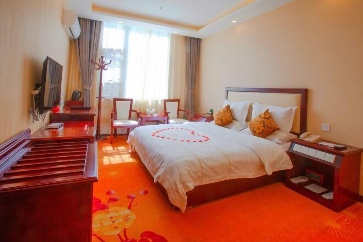 A hotel room with a bed, a desk, a chair, a piano, and a television.