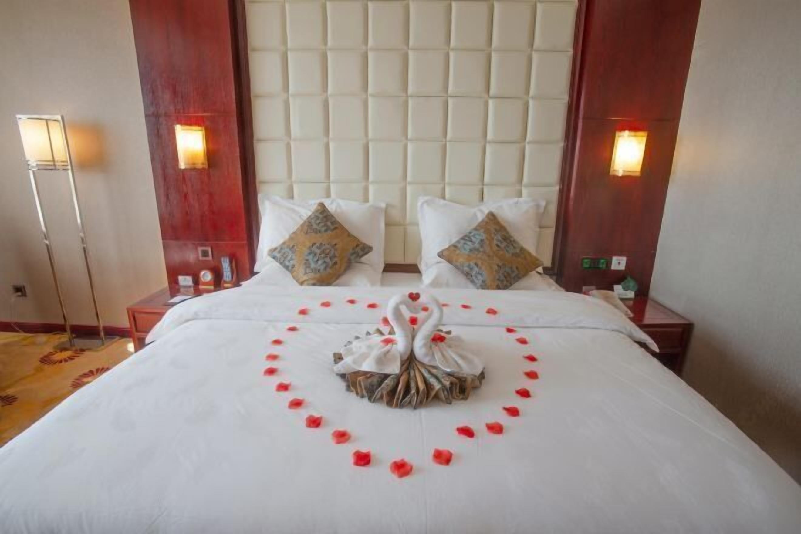 A hotel room with a large bed, two nightstands, a headboard, and wall sconces.
