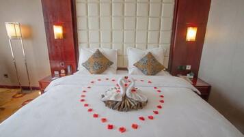 A hotel room with a large bed, two nightstands, a headboard, and wall sconces.