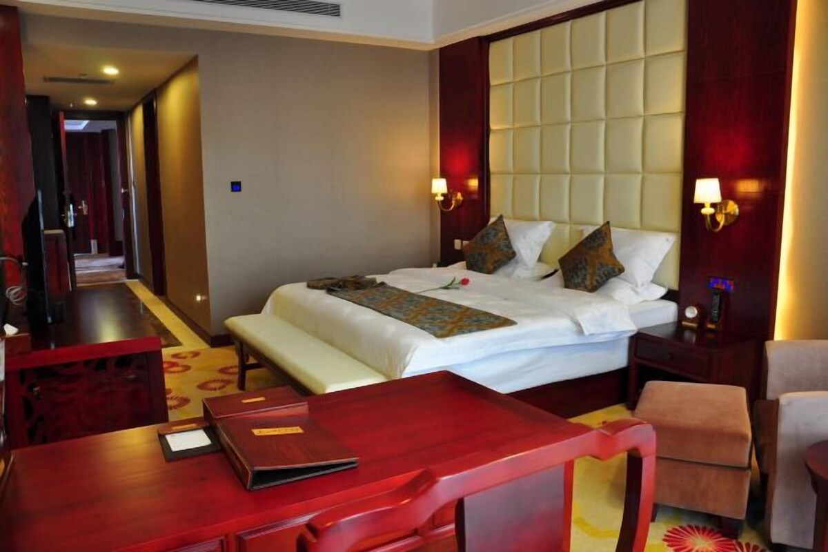 A hotel room with a bed, bedside table, lamp, and a view of the hallway.