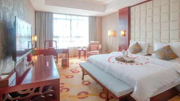 Habitación de hotel con una cama grande, un escritorio, una silla, un televisor y una ventana con cortinas.