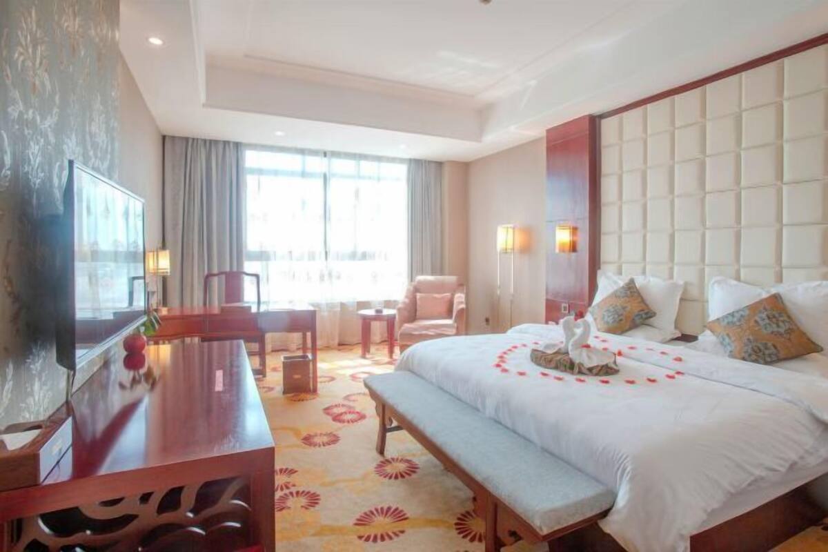 A hotel room with a large bed, a desk, a chair, a TV, and a window with curtains.