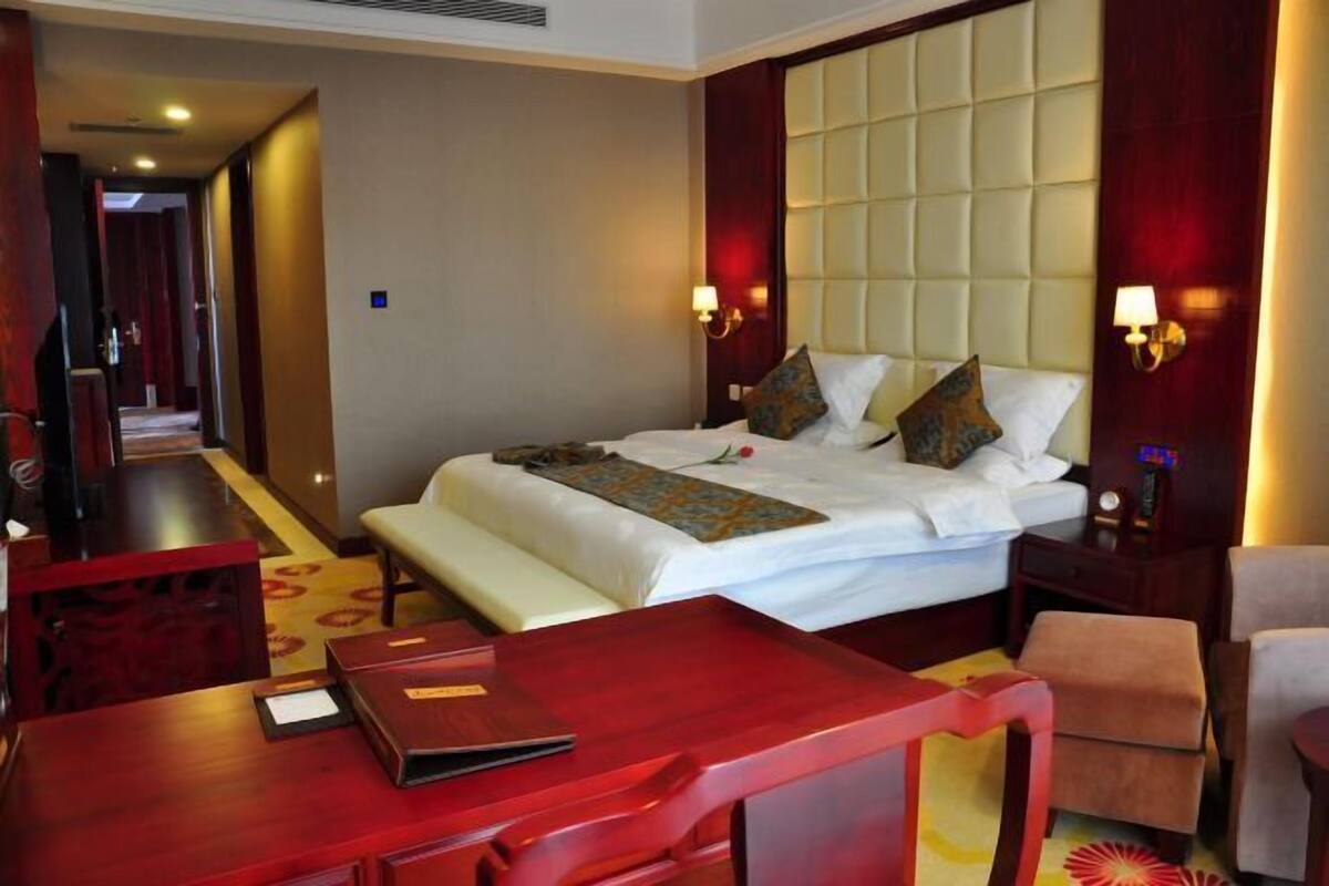 A hotel room with a large bed, a desk, a chair, and a small table.
