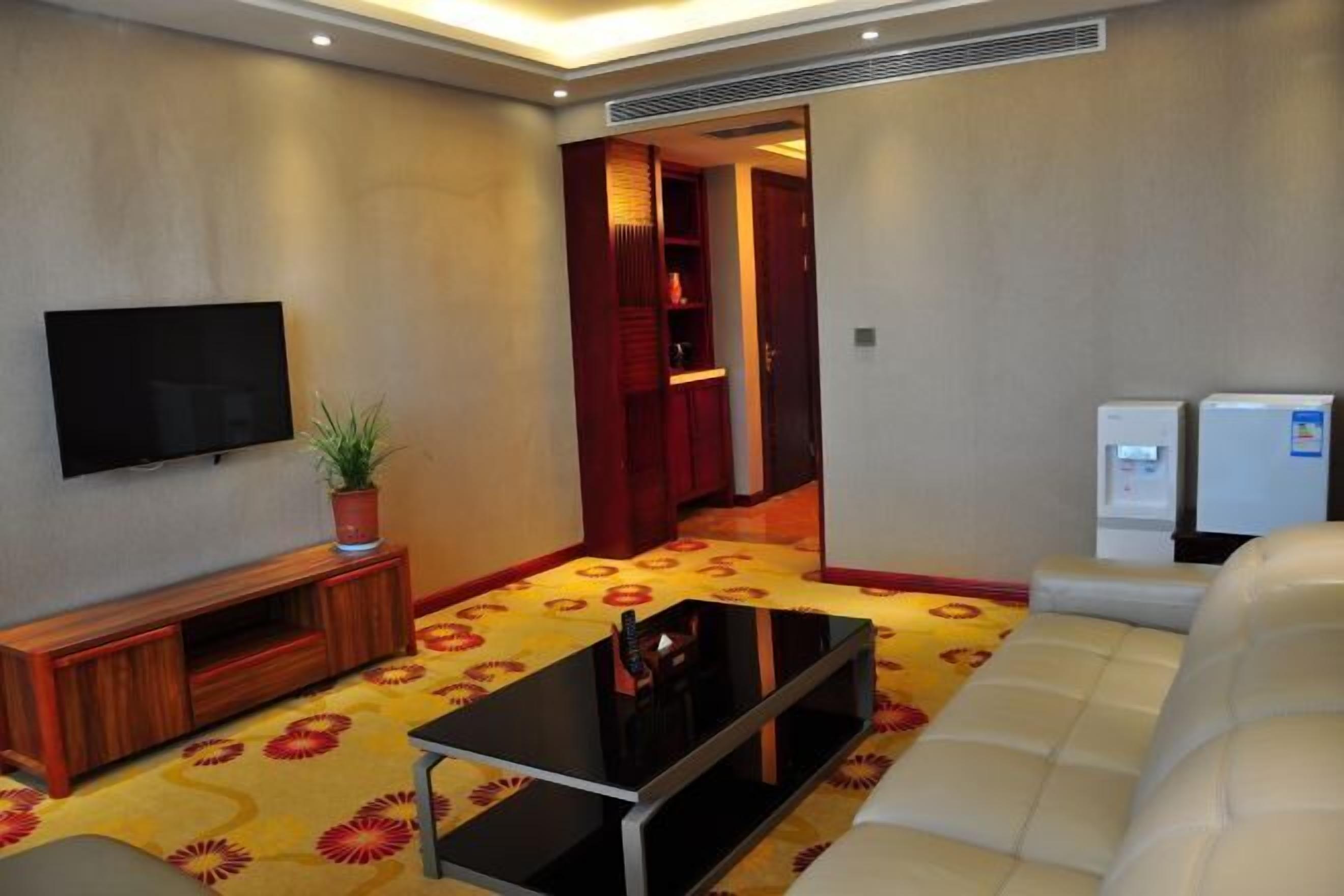A living room with a flat-screen TV, a sofa, a coffee table, a potted plant, and a patterned carpet.