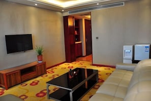 A living room with a flat-screen TV, a sofa, a coffee table, a potted plant, and a patterned carpet. - Jia Li Hotel (Dali)