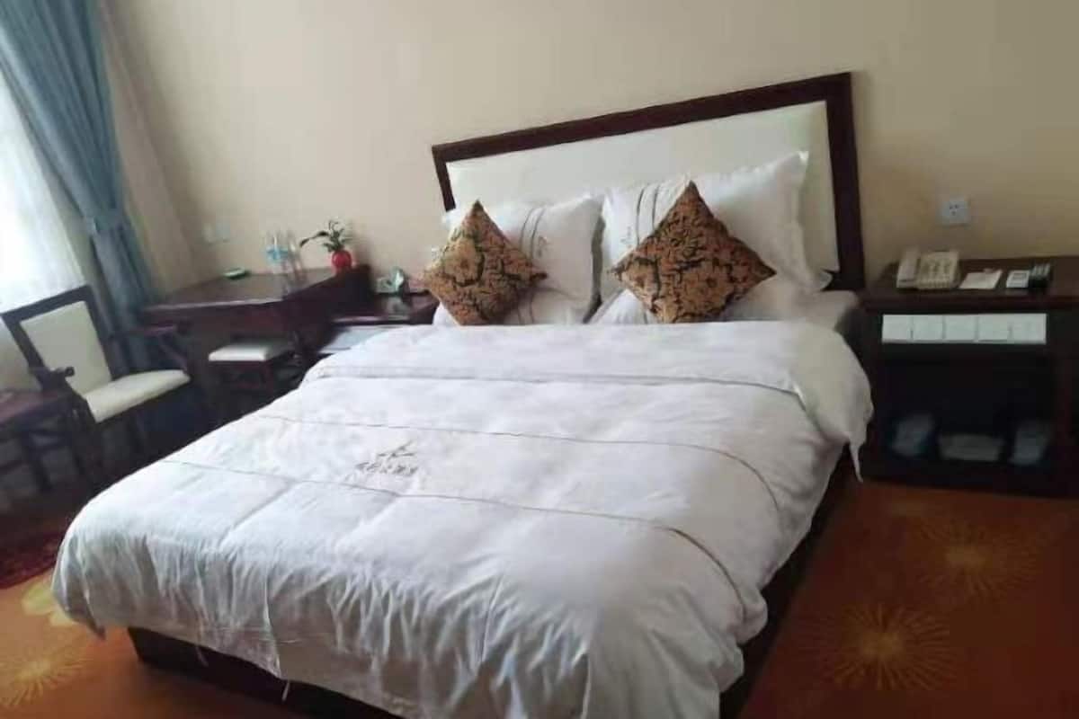 A hotel room with a bed, a desk, a chair, and a nightstand with a phone.