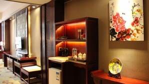 Una habitación de hotel con un escritorio de madera, un televisor, una estantería y un cuadro decorativo.