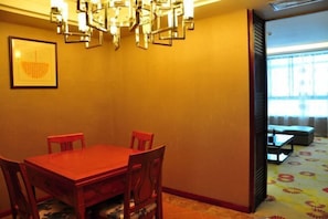 A dining area with a red table and chairs, a chandelier, and a framed artwork on the wall.