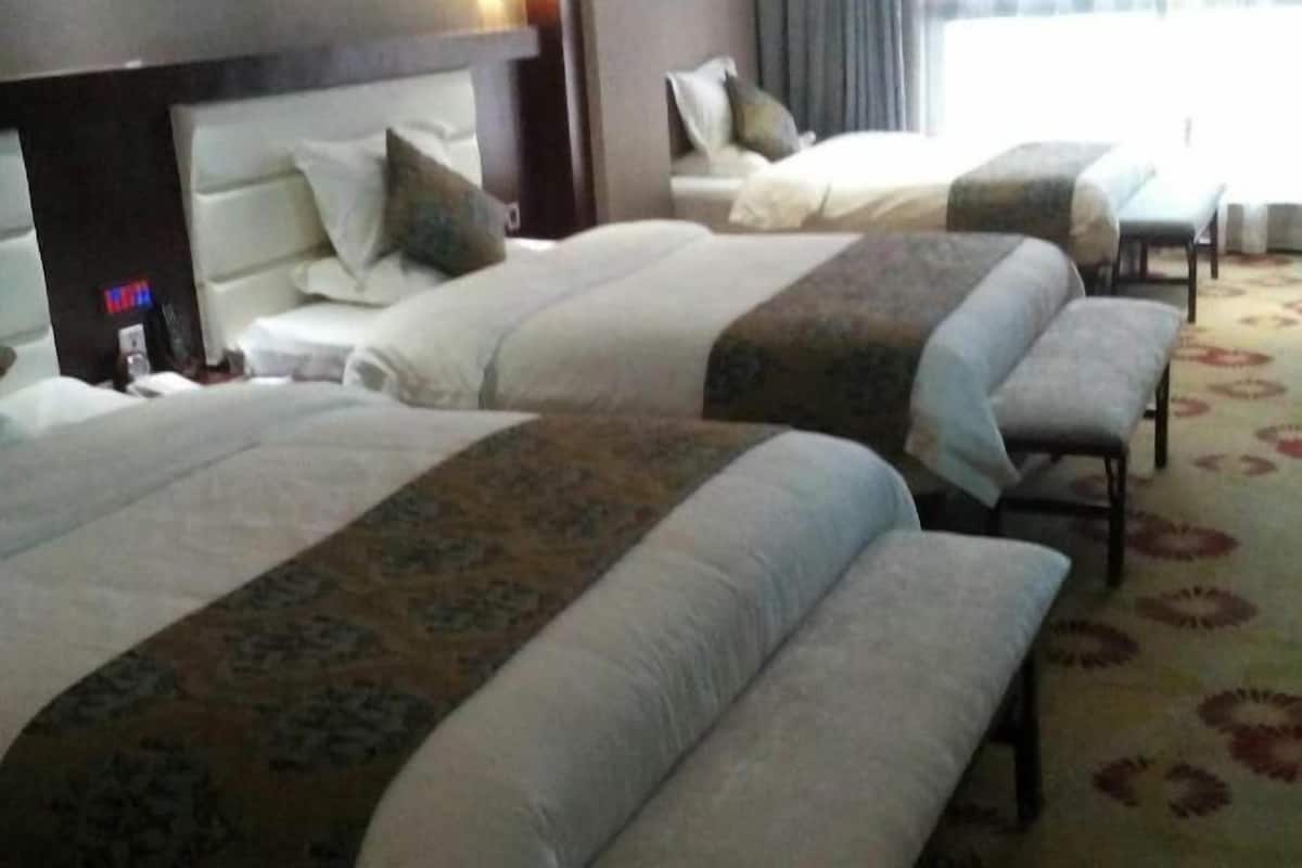 A hotel room with three beds, a headboard, a bedside table, and a patterned carpet.