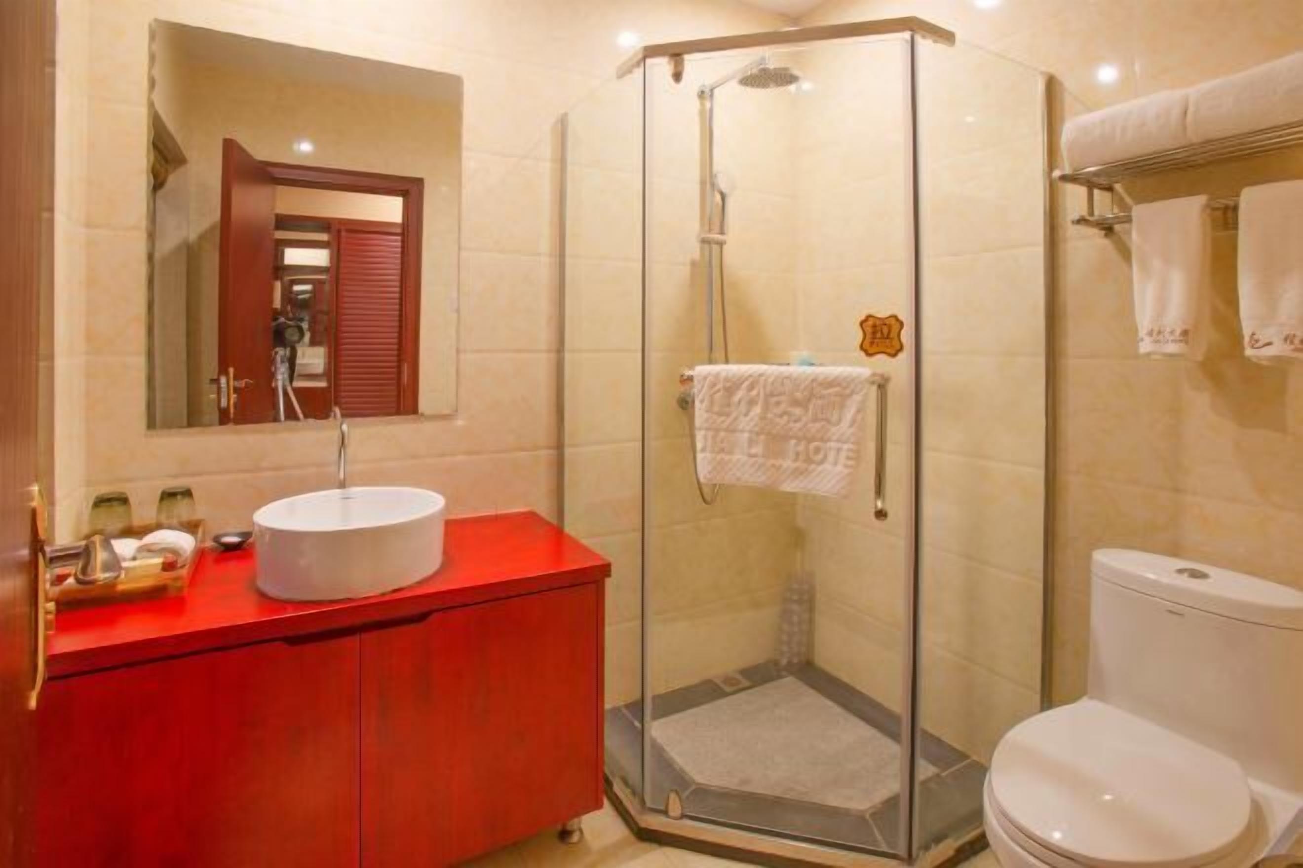 Un baño con ducha de vidrio, un tocador rojo con lavamanos blanco y un inodoro blanco.