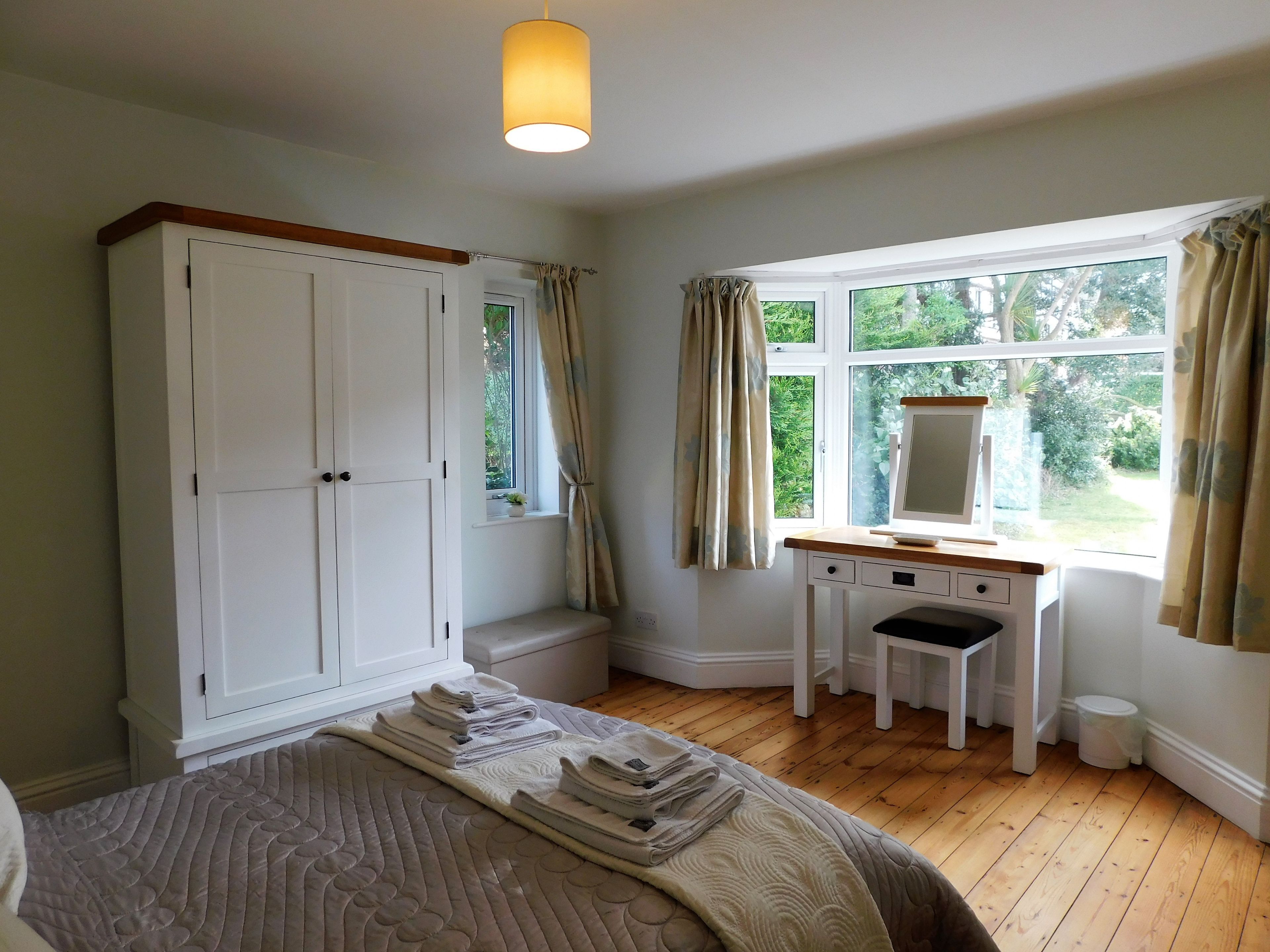 A bedroom with a bed, a desk, a wardrobe, and a window with curtains.
