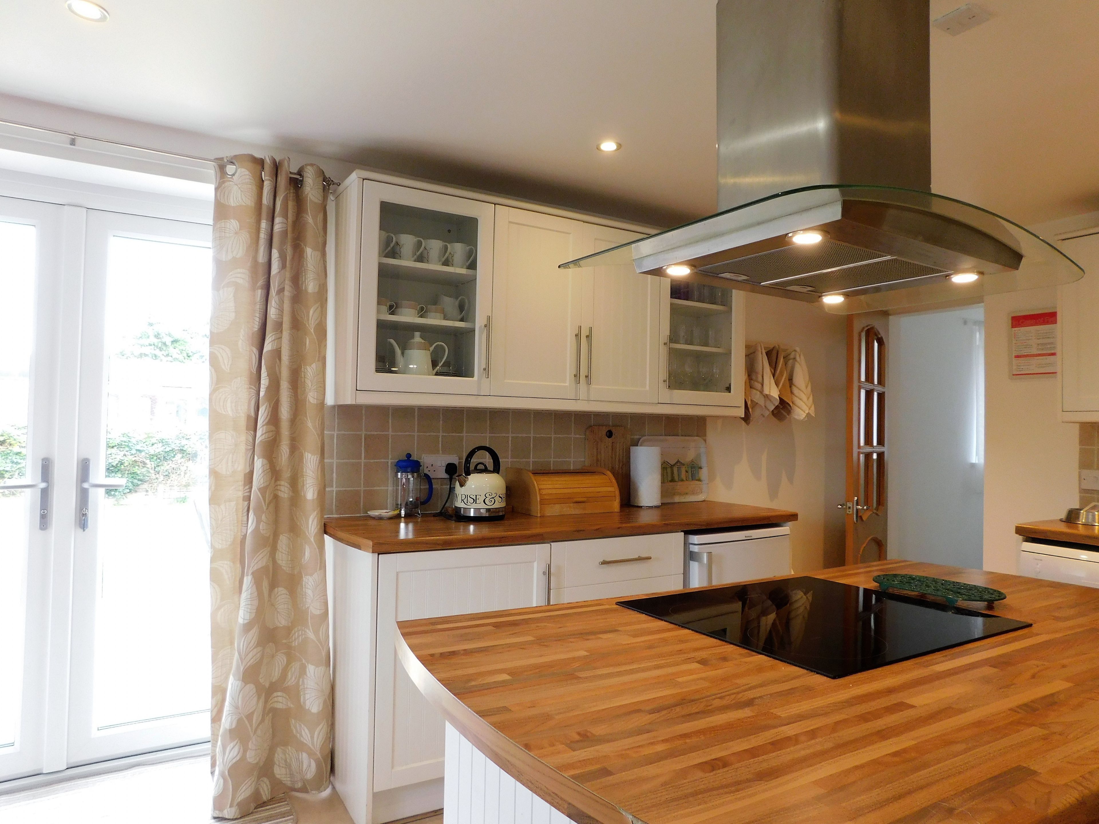 A modern kitchen with white cabinets, a glass-fronted upper cabinet, a stainless steel range hood, and a wooden countertop.