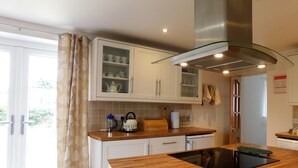Une cuisine moderne avec des armoires blanches, un meuble supérieur à façade en verre, une hotte de cuisinière en acier inoxydable et un plan de travail en bois.