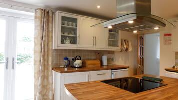 A modern kitchen with white cabinets, a glass-fronted upper cabinet, a stainless steel range hood, and a wooden countertop.