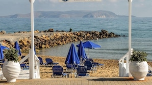 Un café de playa con un letrero que dice "Dos Palmas Beach Cafe", con una pérgola blanca, sombrillas azules y sillas de playa.