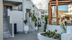 Un edificio moderno con paredes blancas, una pérgola de madera y un patio empedrado con plantas en macetas.