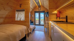 A wooden cabin with a bed, a small kitchenette, and a sliding glass door leading to an outdoor area. - Loch Ewe Luxury Pods (Achnasheen)