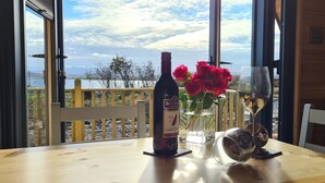 A table with a wine bottle, a glass, and a vase of red roses. - Loch Ewe Luxury Pods (Achnasheen)