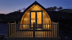 A wooden cabin with a balcony, set against a hilly backdrop. - Loch Ewe Luxury Pods (Achnasheen)