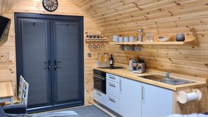 A compact kitchen with a wooden interior, a sink, a coffee maker, and a stove. - Loch Ewe Luxury Pods (Achnasheen)
