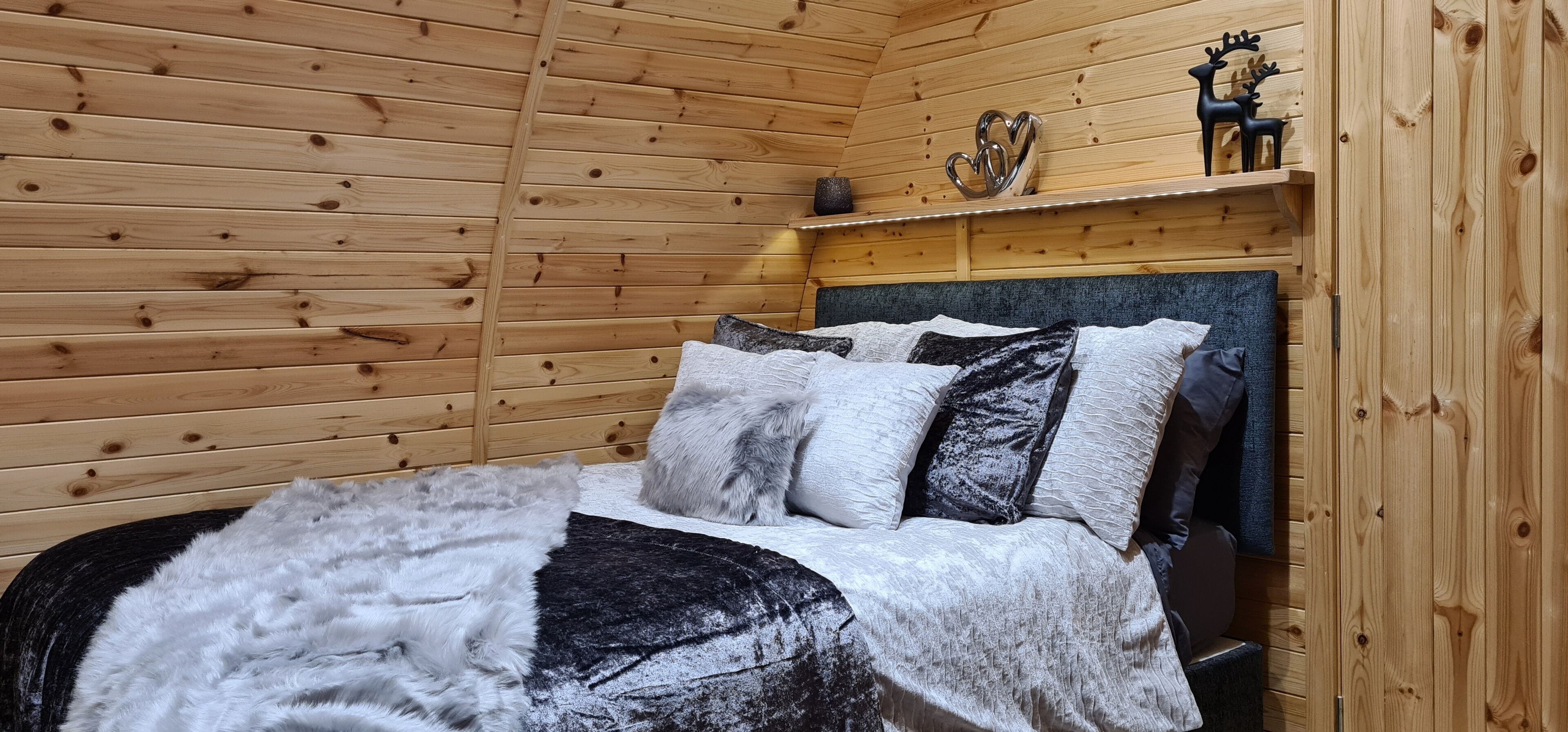 A wooden-paneled room with a bed, pillows, and a shelf with decorative items.